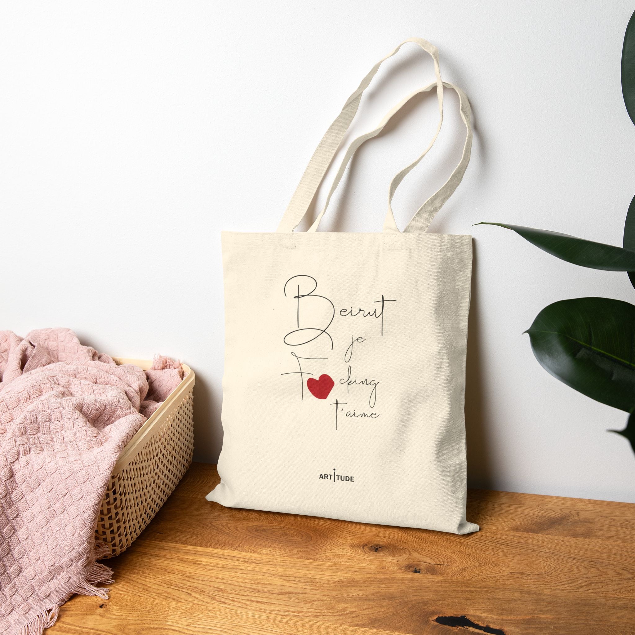 Beirut tote bag with text and a heart design on a wooden surface with a white wall and plant in the background.