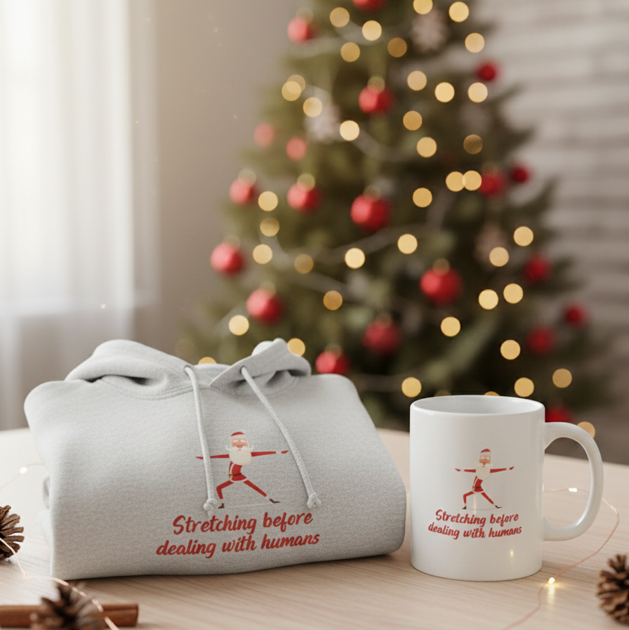 Gray hoodie and white mug with text in front of a decorated Christmas tree.