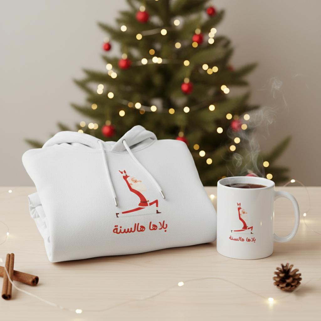 White hoodie and mug with red design in front of a decorated Christmas tree.