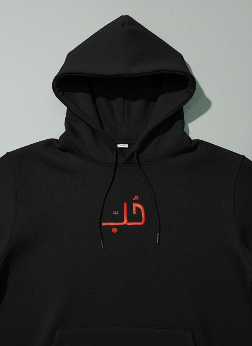 Black hoodie with embroidered  red Arabic text on a light gray background