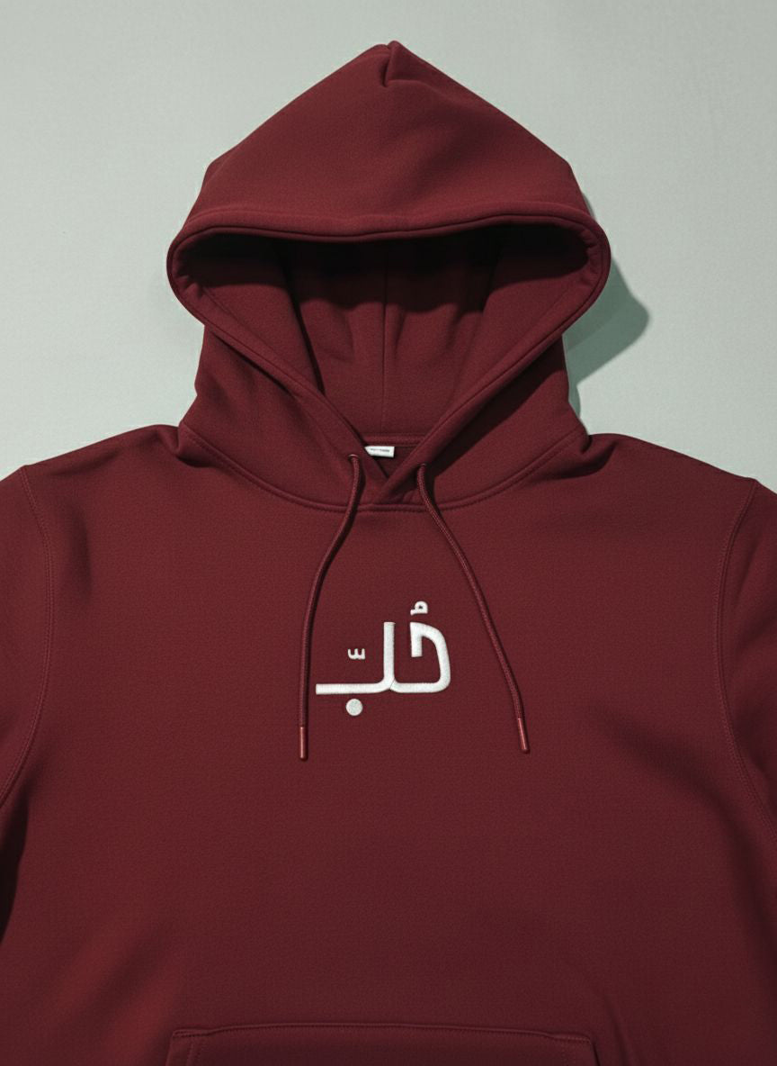 Maroon hoodie with embroidered  Arabic text on a light gray background