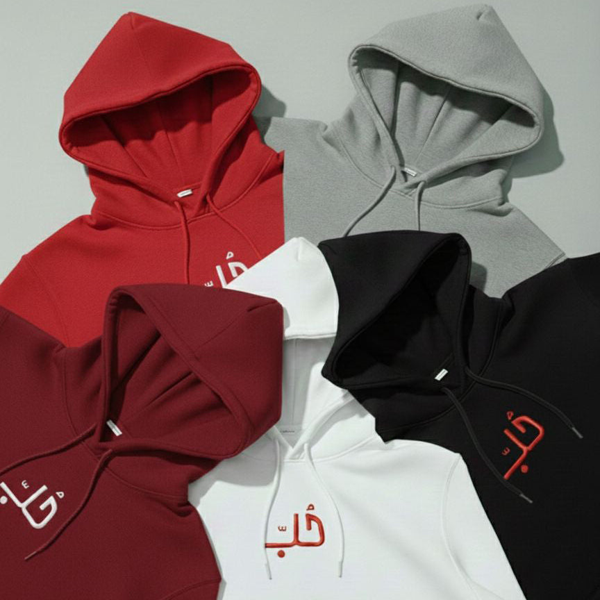 Collection of hoodies in red, gray, bordeaux, white, and black with Arabic text a light gray background.