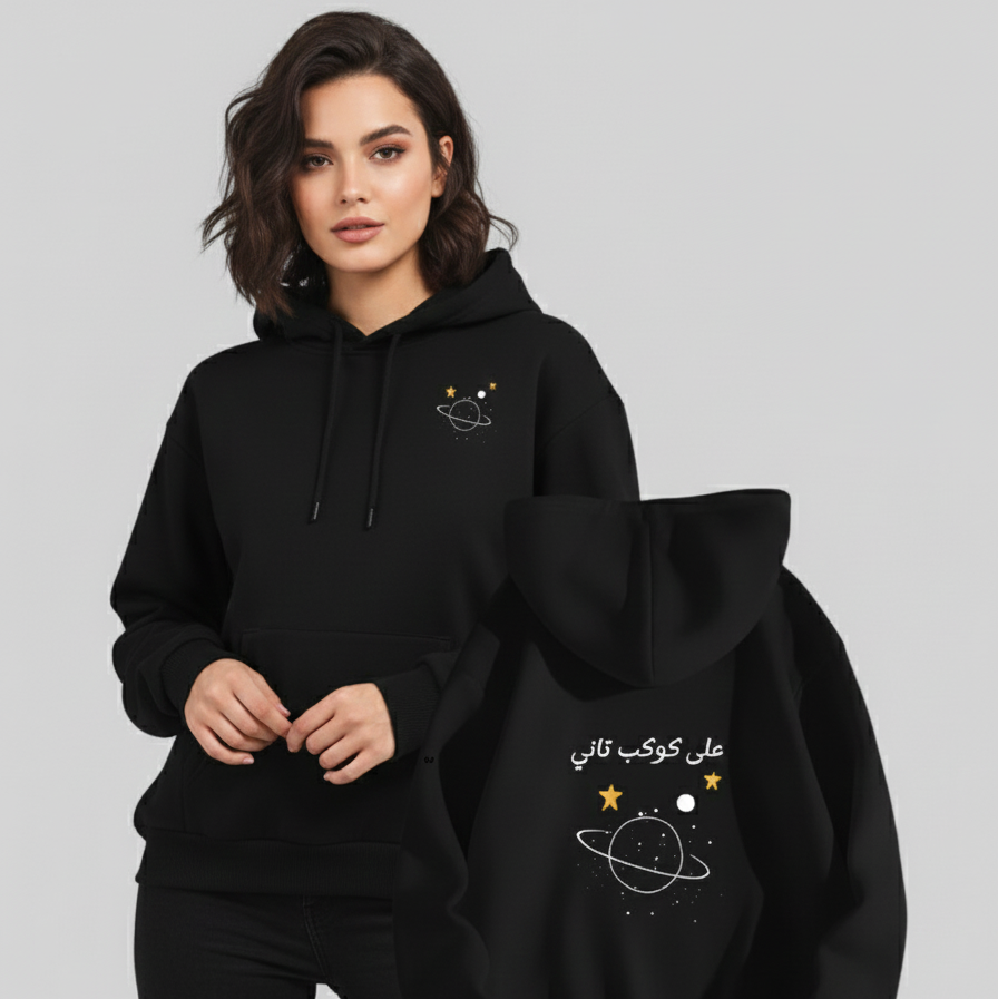 Woman wearing a black hoodie with space-themed design, holding another black hoodie with similar design.