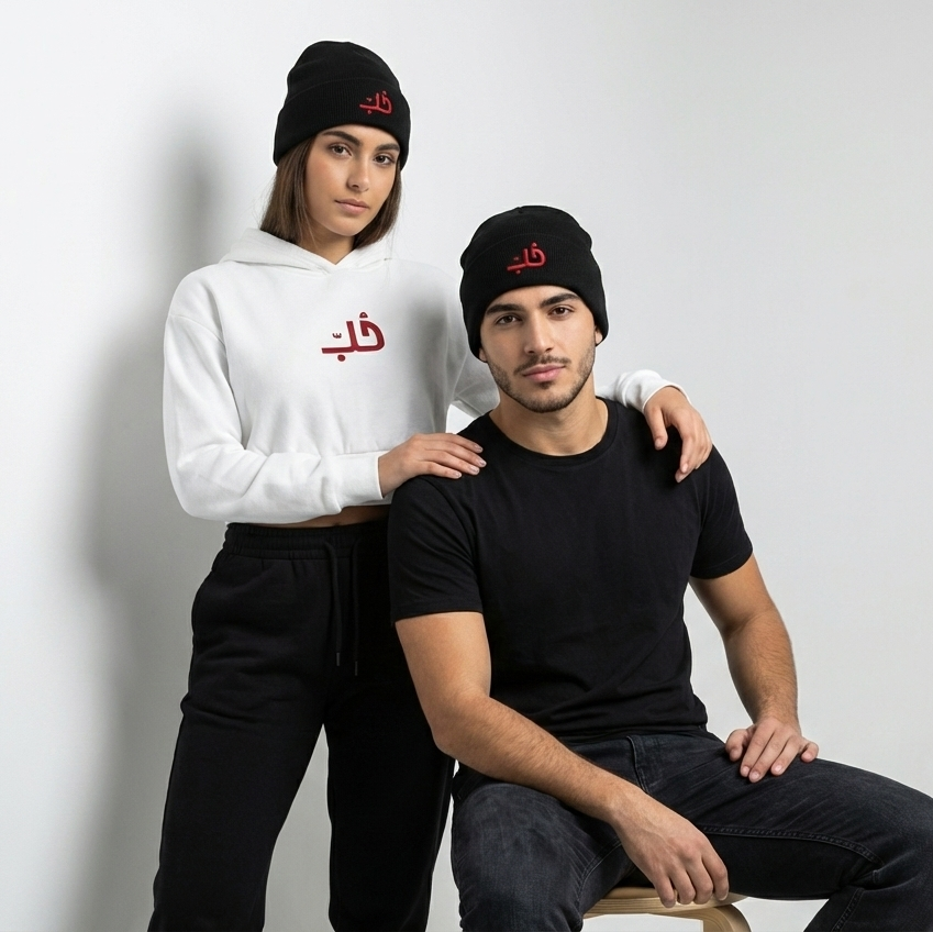 Two people wearing black beanies and clothing with Arabic text on a white background