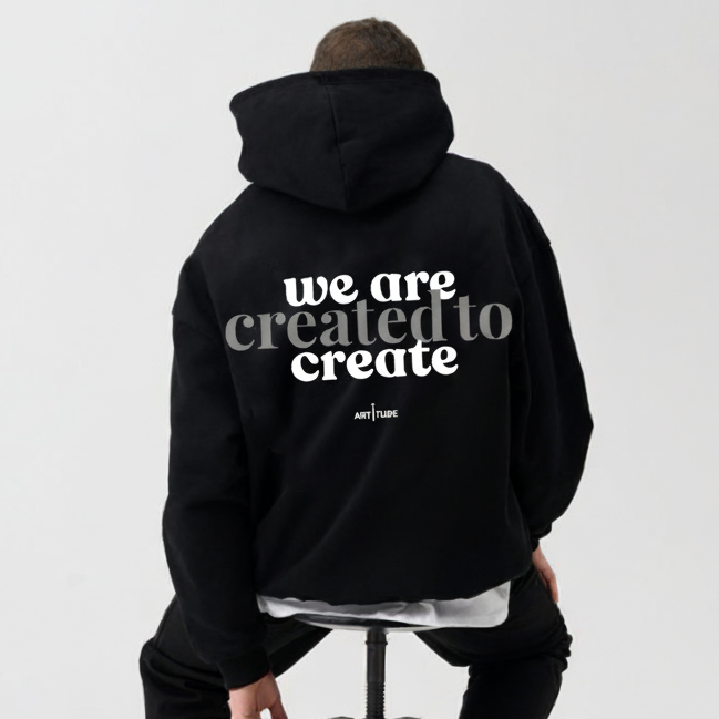 Person wearing a black hoodie with 'we are created to create' text on a white background.