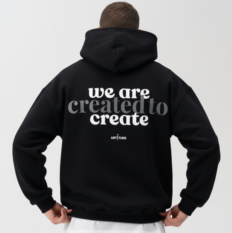 Person wearing a black hoodie with 'we are created to create' text on the back, on a white background.
