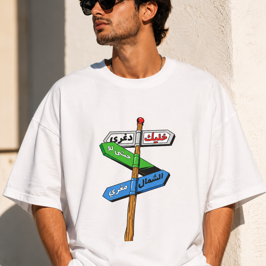 Man wearing a white t-shirt with a colorful graphic design against a light-colored wall.