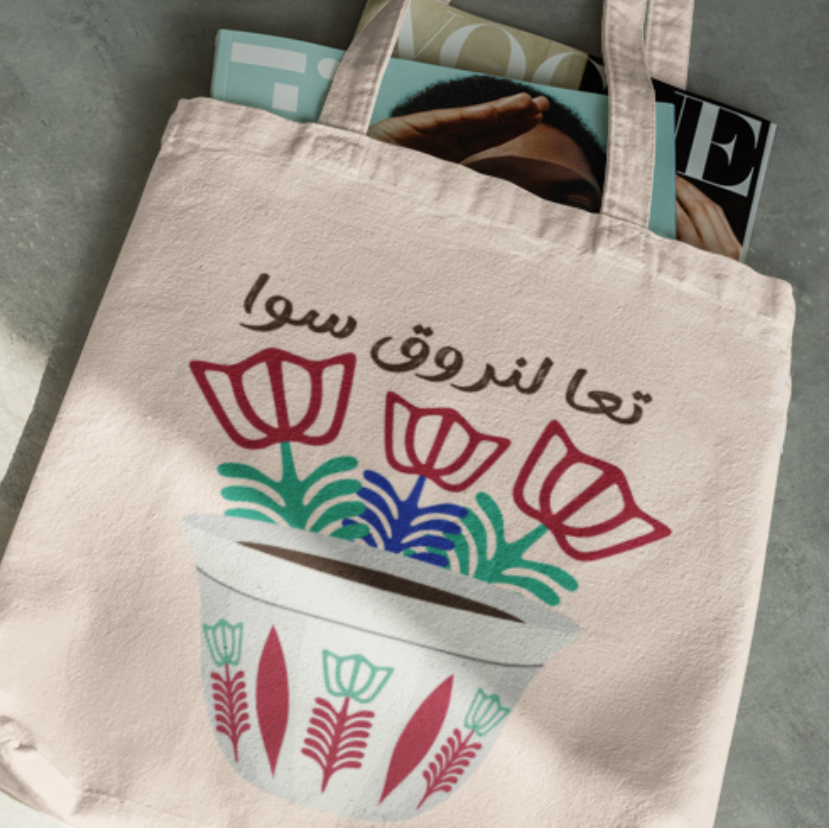 Beige tote bag with floral design and Arabic text on a gray surface