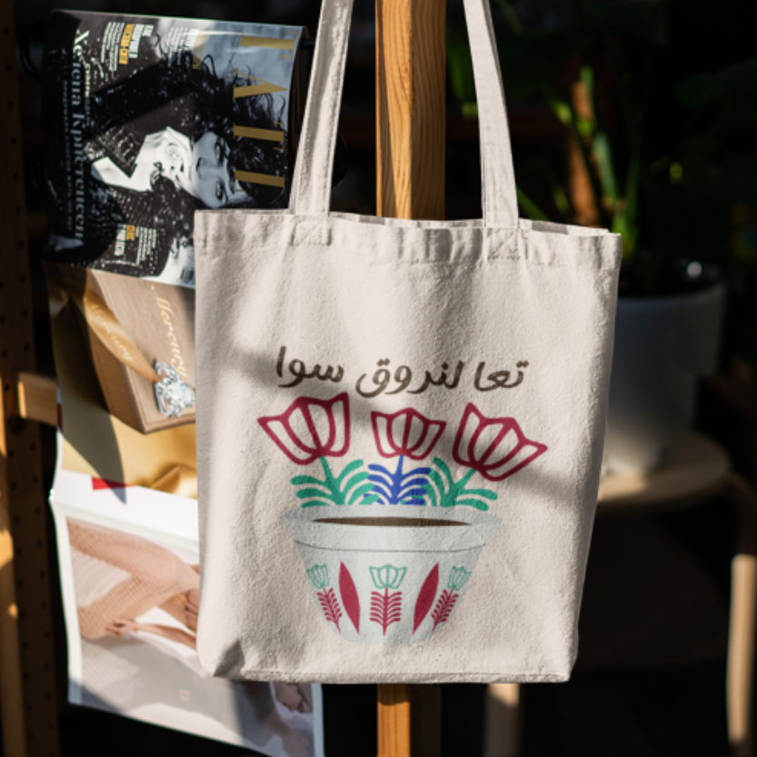 Tote bag with Arabic text and colorful design hanging on a rack.